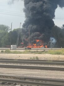 Firefighters spray water onto a fire burning near railroad tracks west of the Grain Craft facility on 30th Street on Tuesday, Aug. 26, 2025.